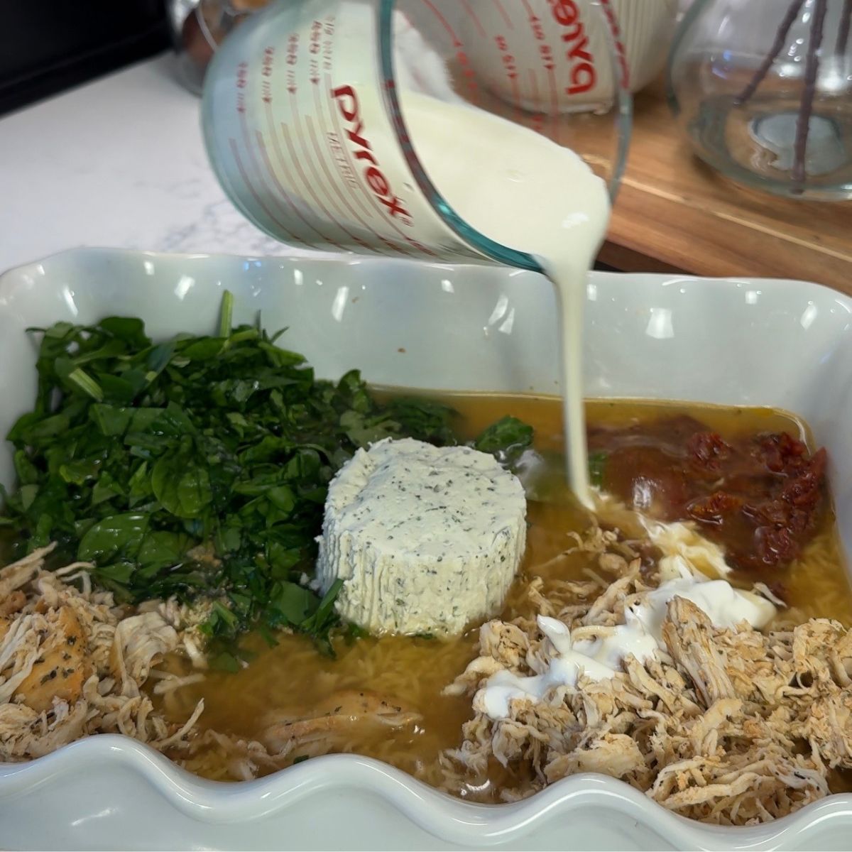 dish with ingredients in pan with hand holding cup with cream pouring over dish