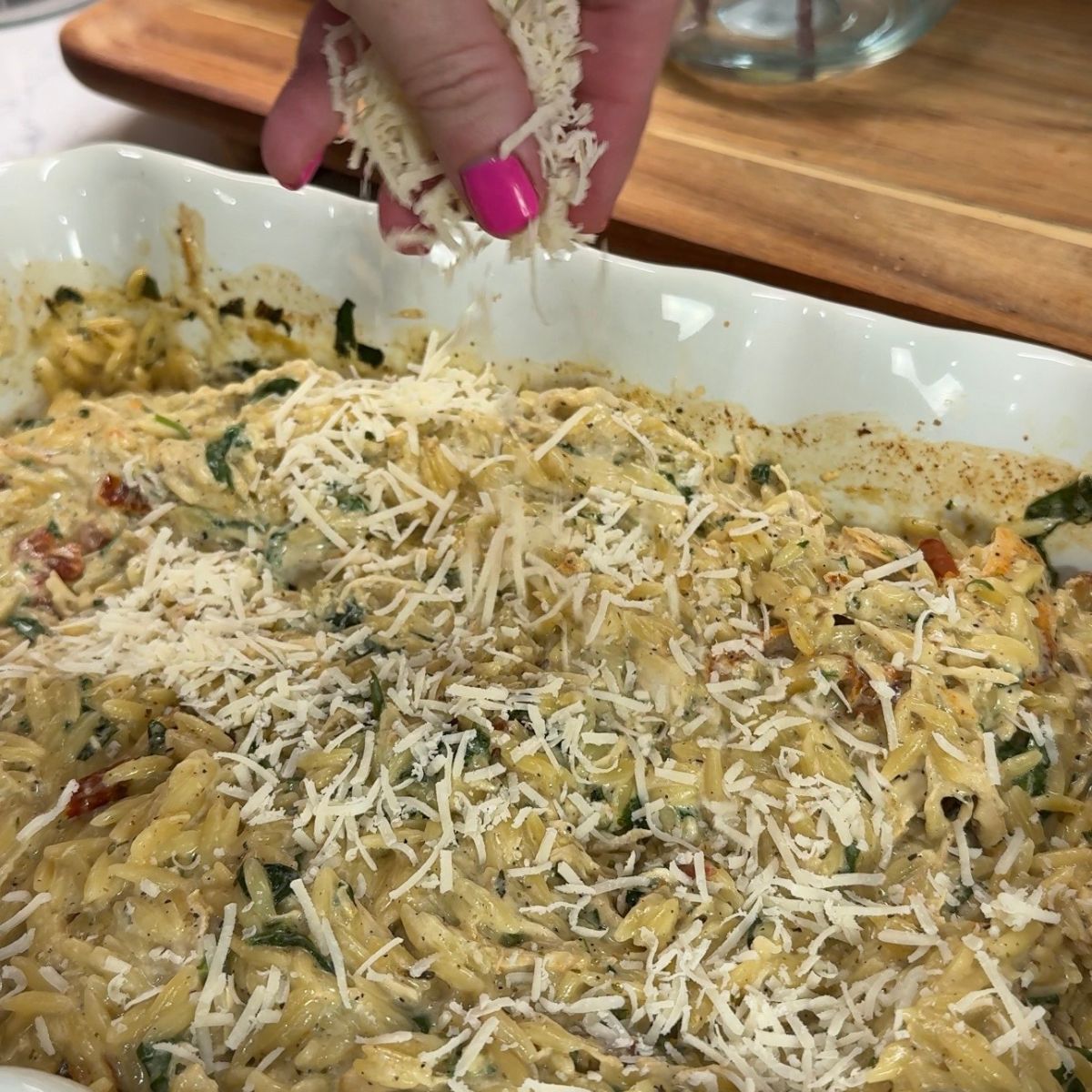 hand pouring shredded parmesan cheese over cooked pasta bake