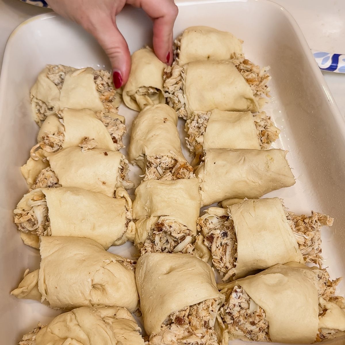 chicken alfredo crescent casserole layered on bottom of dish. hand holding crescent dough