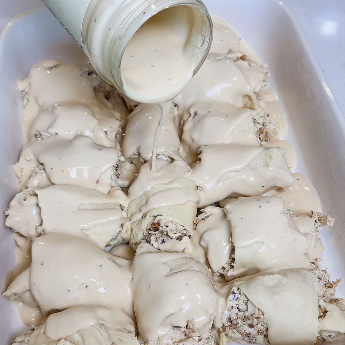 chicken alfredo crescent roll casserole in pan with alfredo sauce poured on top of crescent dough