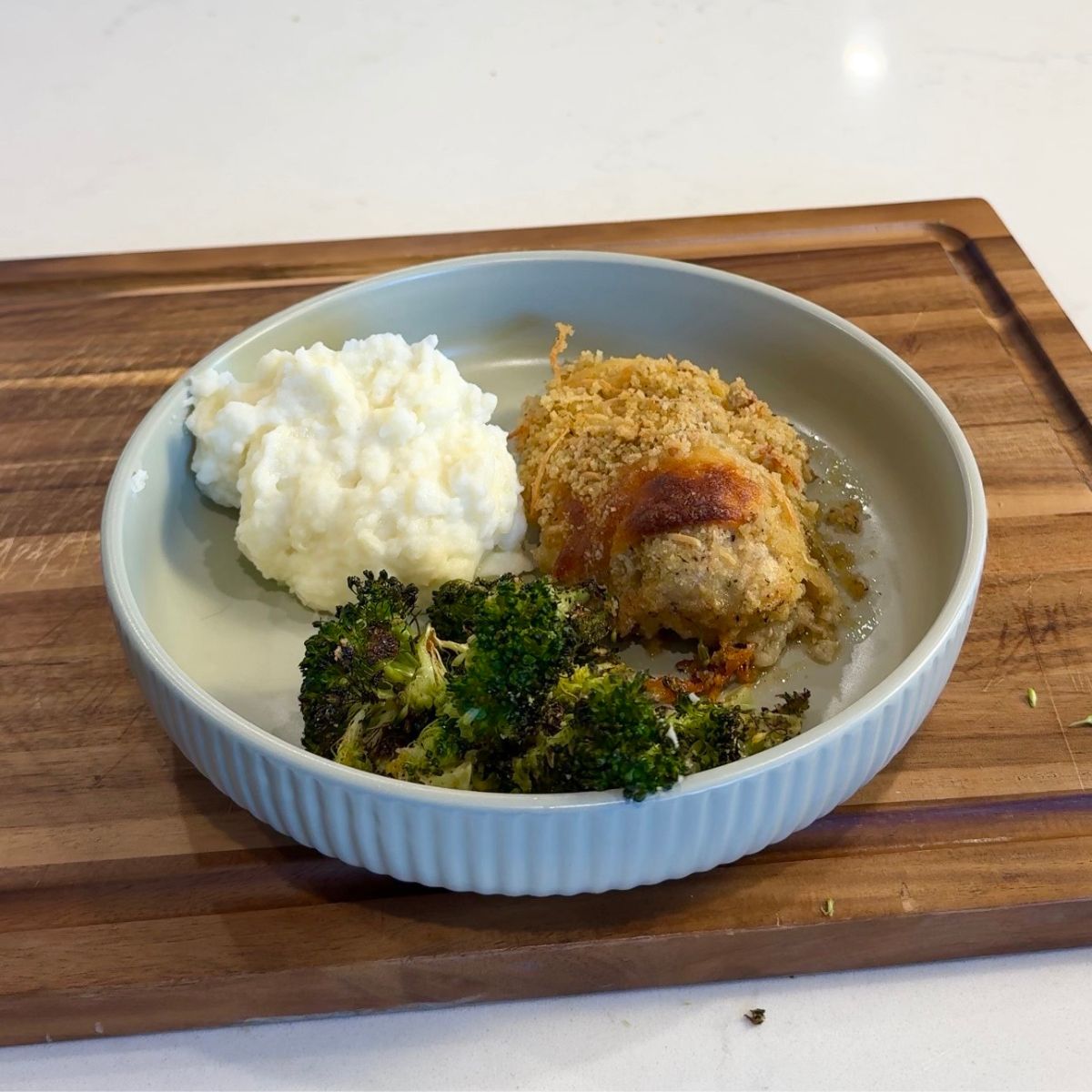 chicken caesar bake with mashed potatoes, broccoli on green plate with wooden board underneath