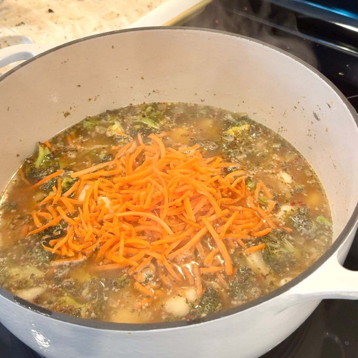 broccoli cheddar gnocchi soup with broccoli and carrots with liquid showing at the top of large pot