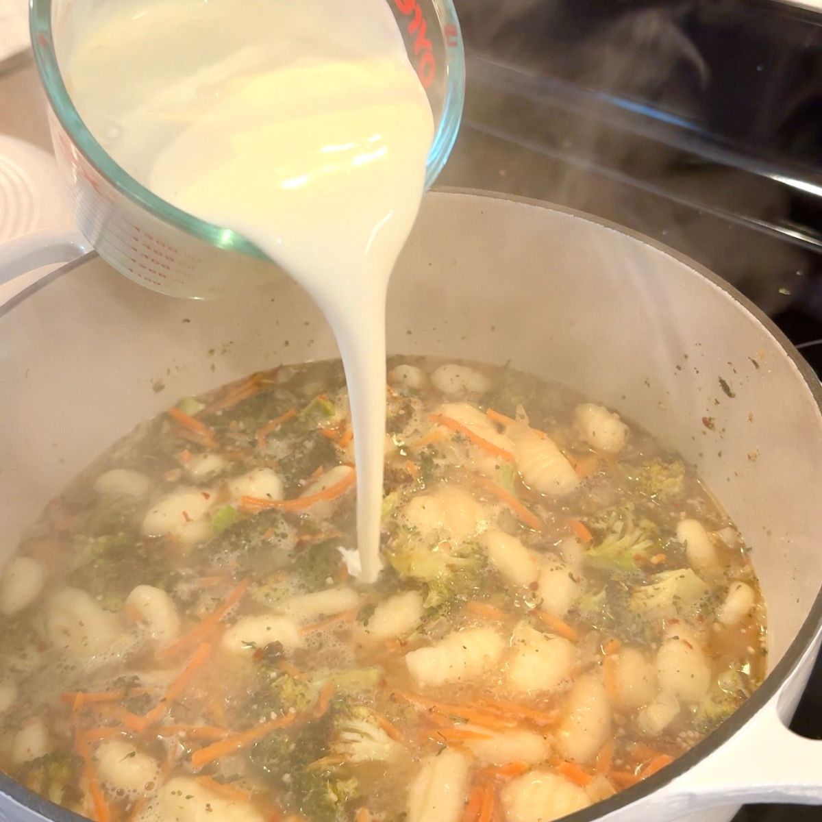 heavy cream being poured into dutch oven for broccoli cheddar gnocchi soup