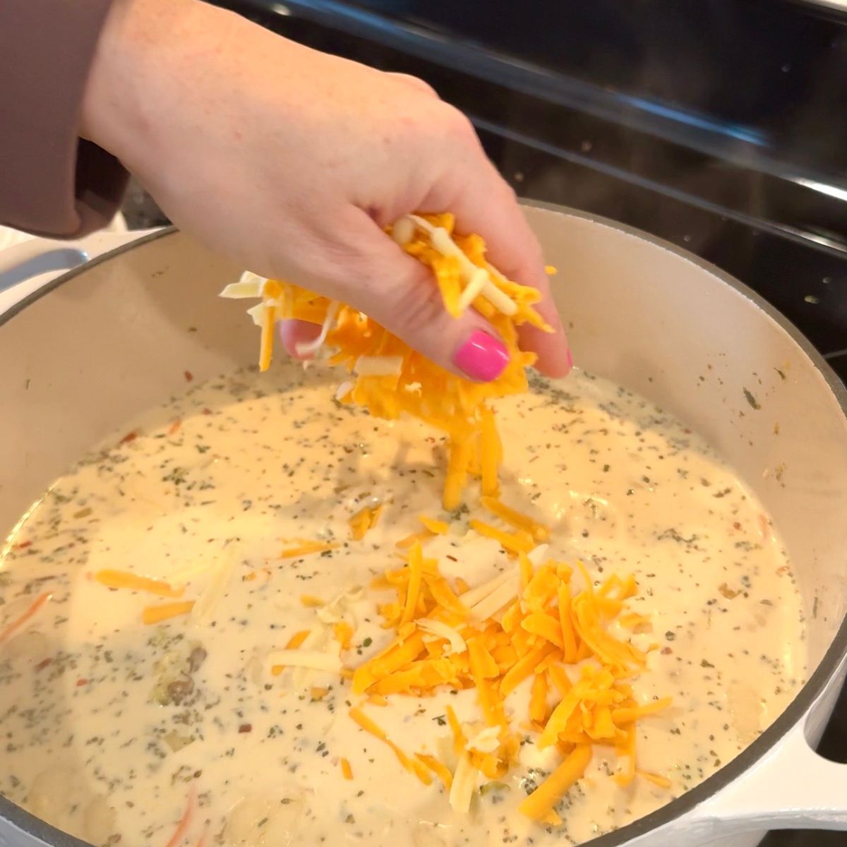 hand putting cheese in dutch oven for soup
