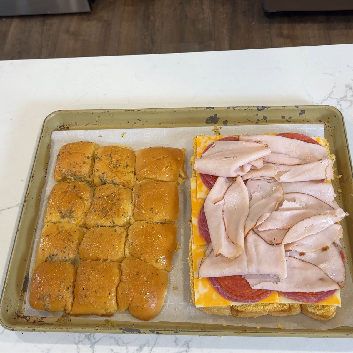 sliced mini bread rolls with layers of cheese, salami, pepperoni, and turkey breast on tray