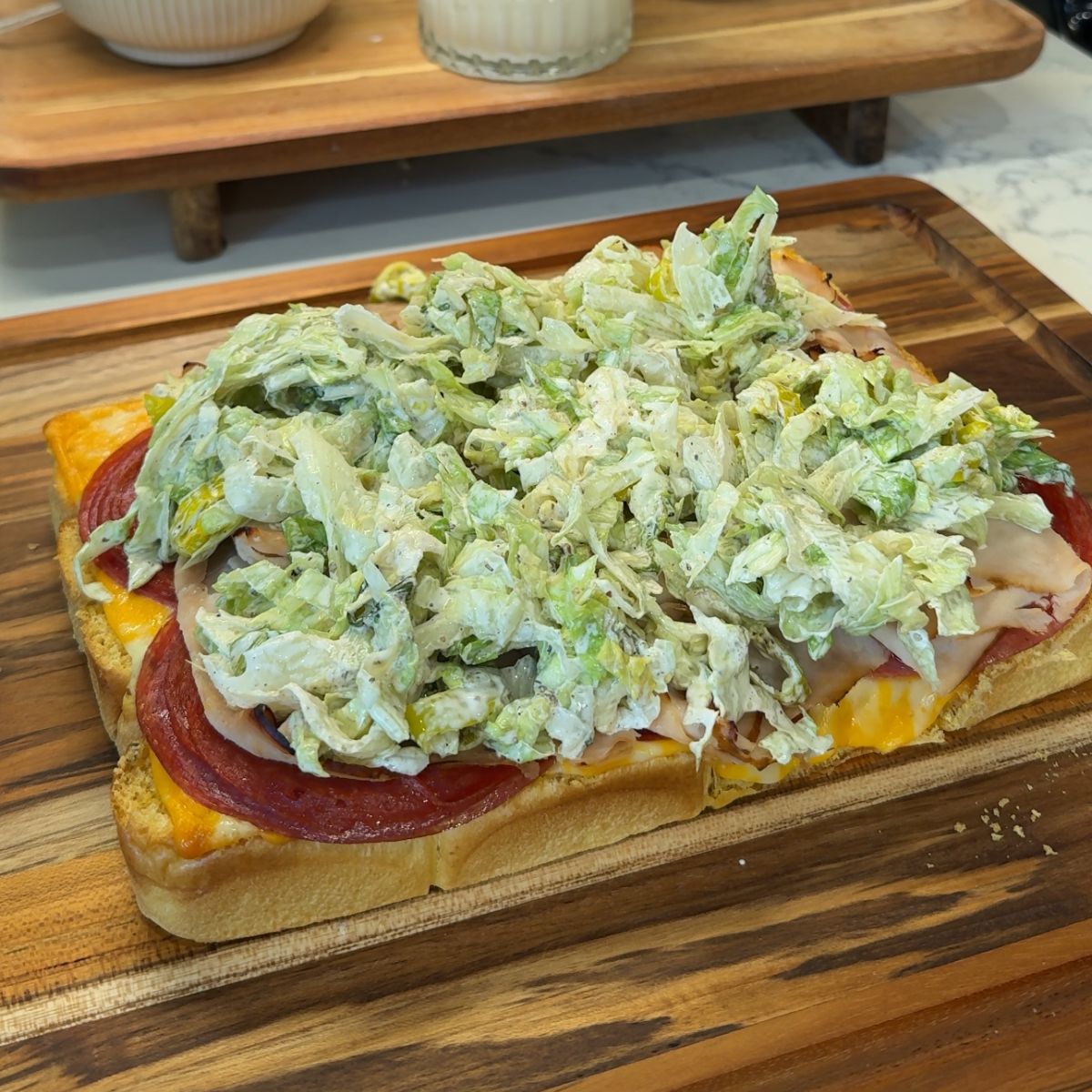 italian grinder sliders on wooden board with layers of cheese, meat, and salad topper