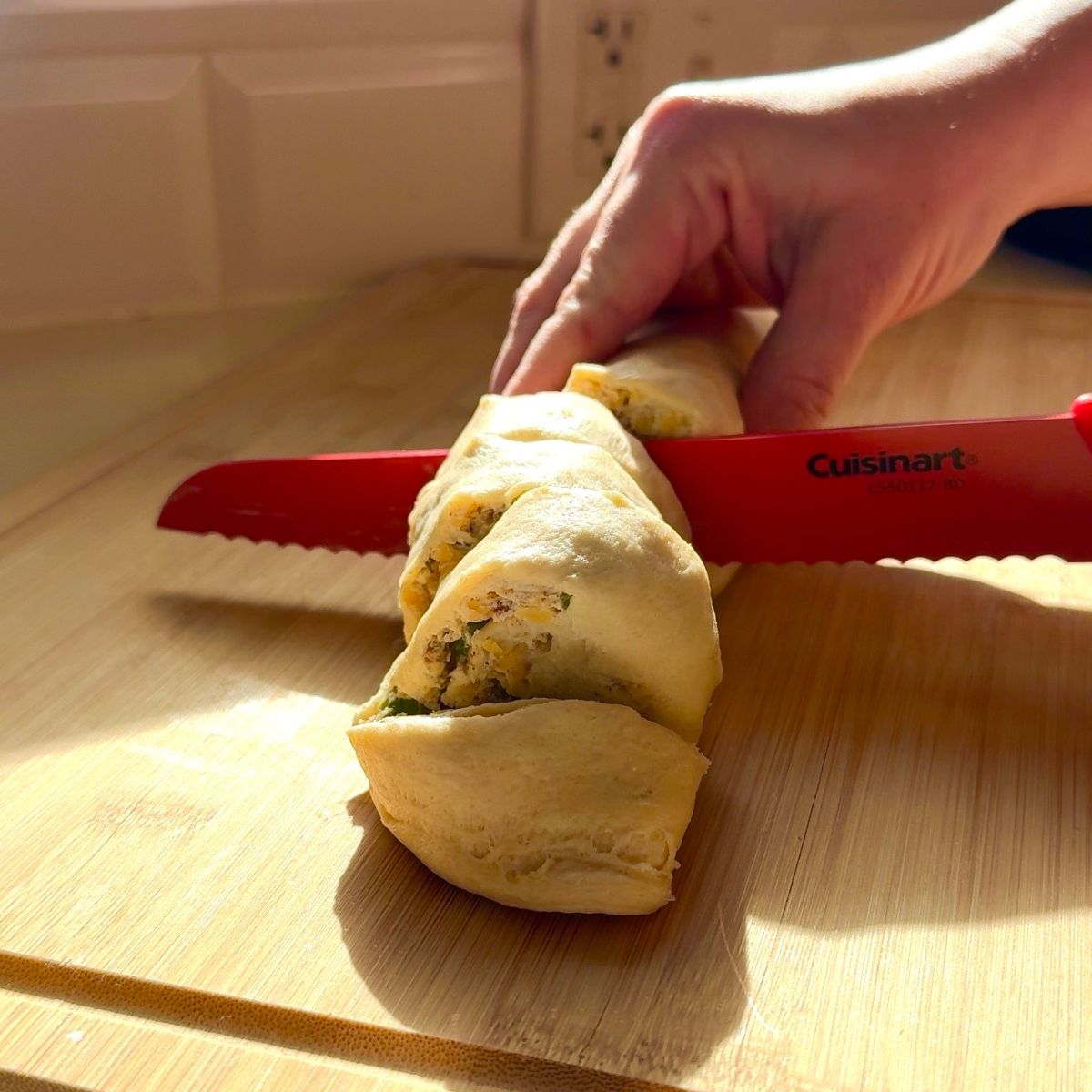rolled crescent dough being cut into slices with hand holding knife