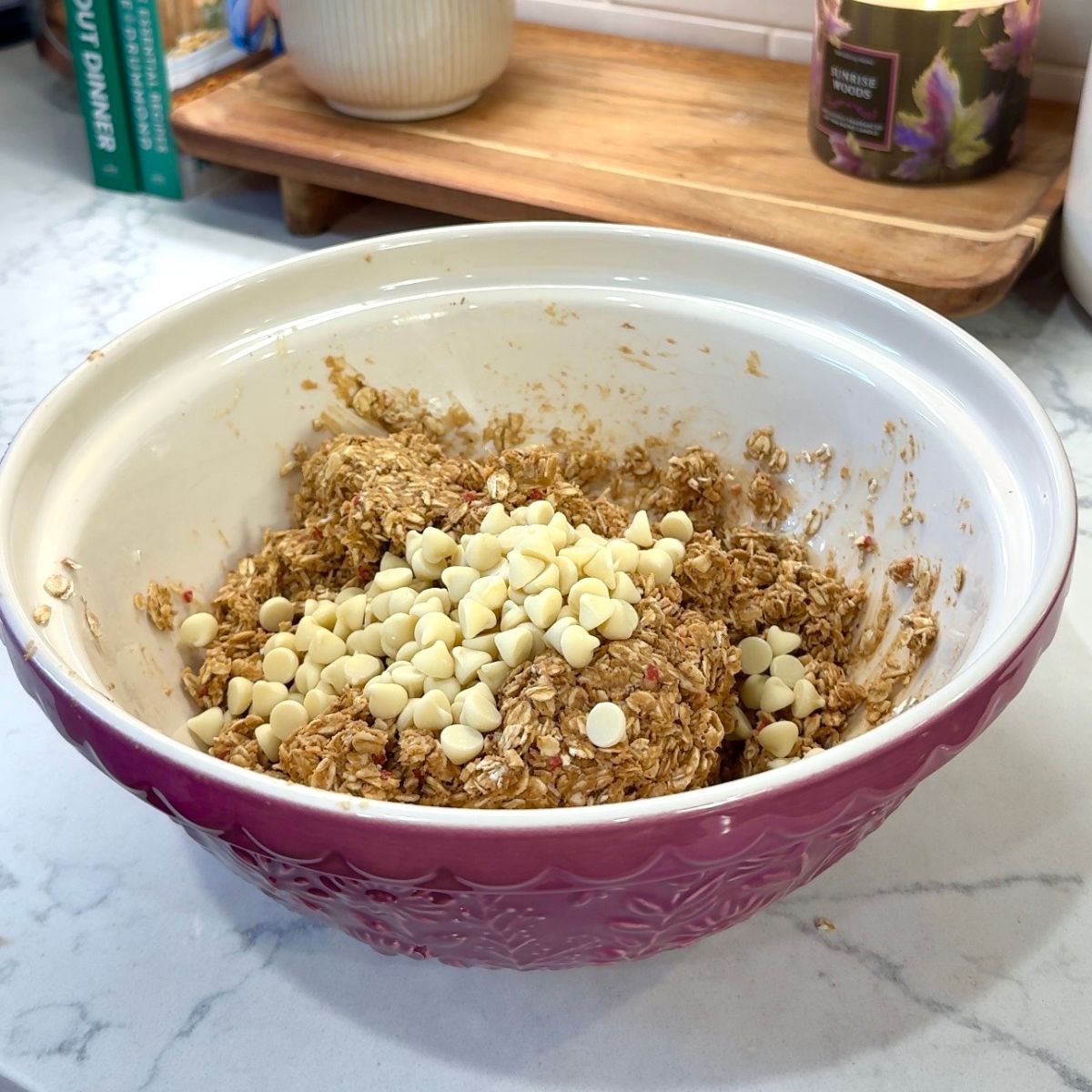 white chocolate chips added into no bake energy bites ingredients in pink mixing bowl