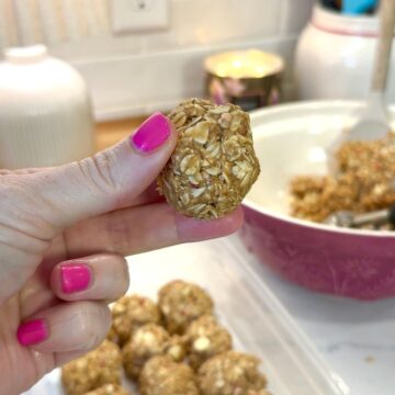 no bake white chocolate energy bites in background. hand with pink nail polish holding one