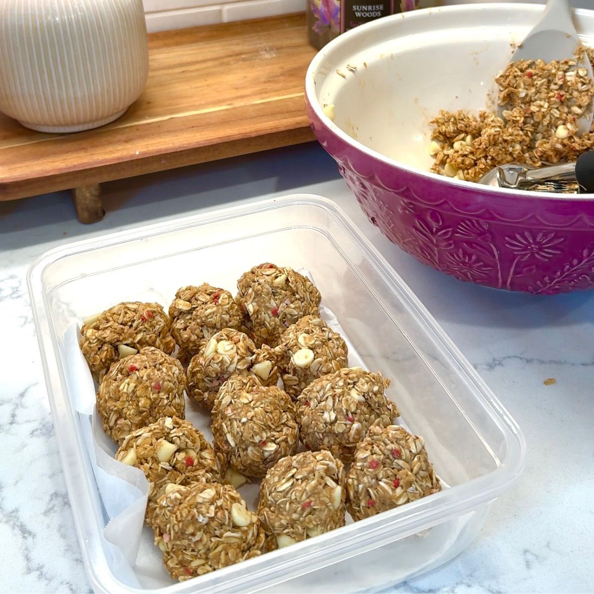 white chocolate no bake energy bites in container, with pink bowl to the side with remaining dough