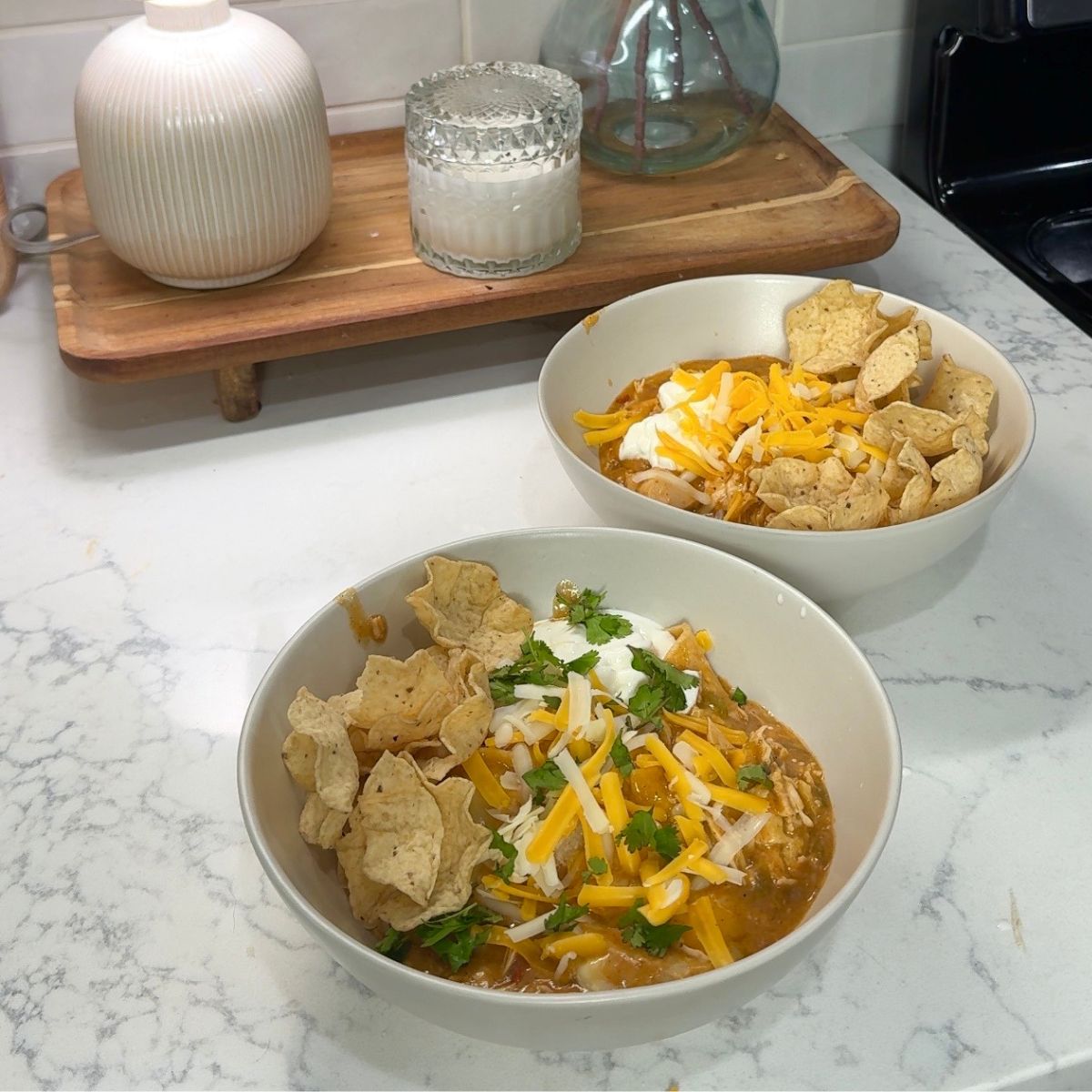 chicken enchiladas in two bowls with chips and cheese on top. lamp and candle in background