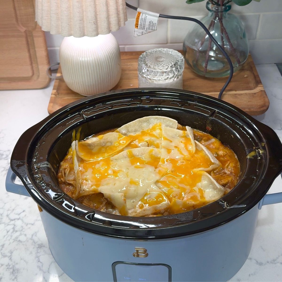 finished dinner with melted cheese and tortillas showing in blue colored slow cooker. lamp in background