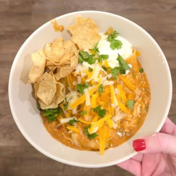 slow cooker chicken enchiladas with hand holding bowl