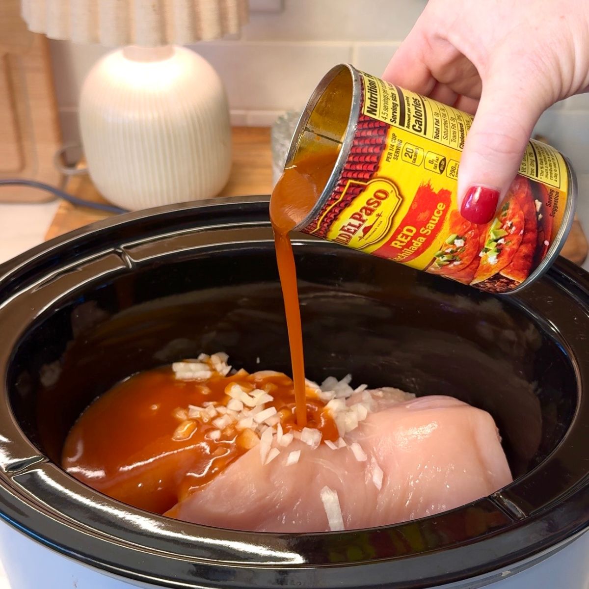 red enchilada sauce pouring into dish with chicken and onions