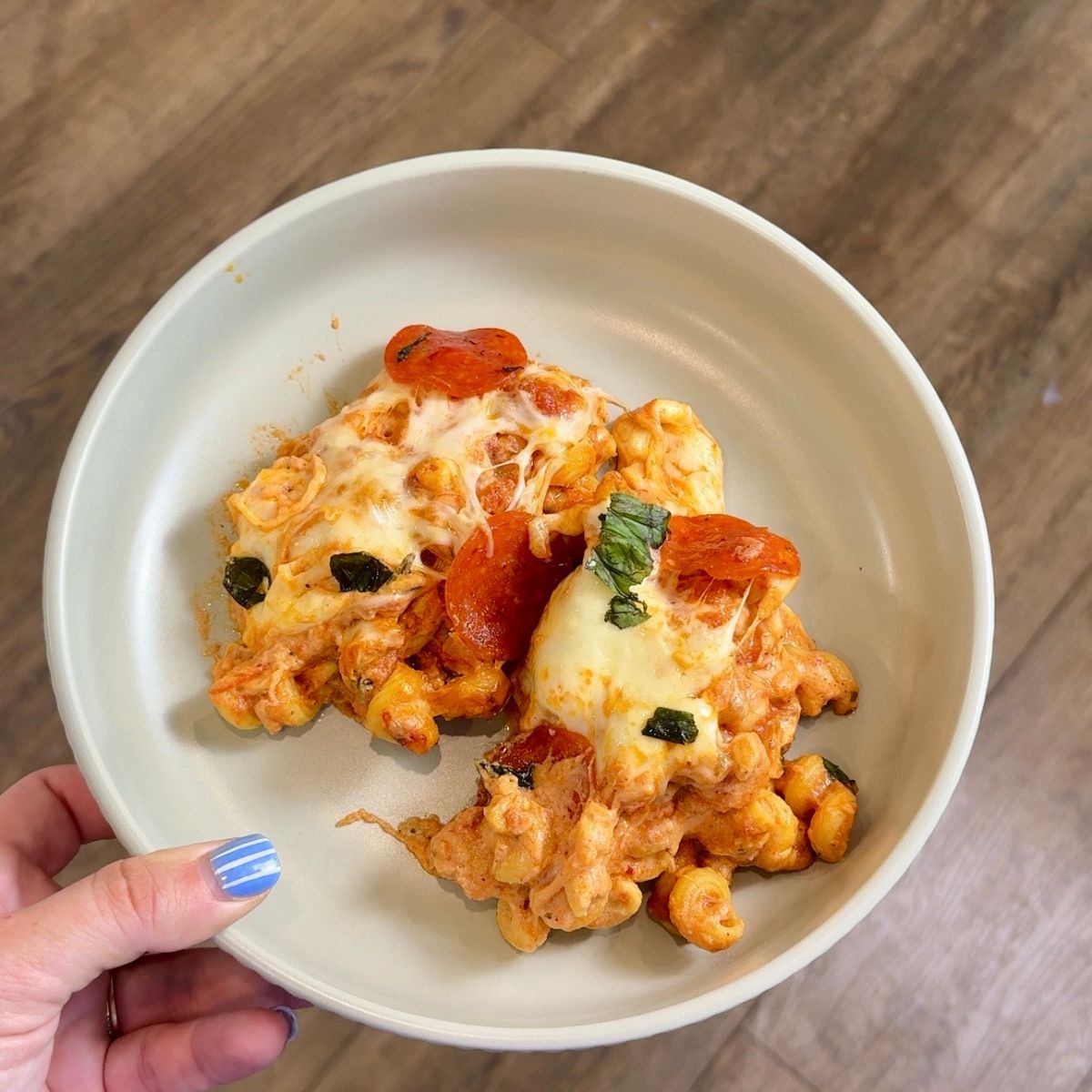 pizza pasta bake on green plate and hand holding the plate