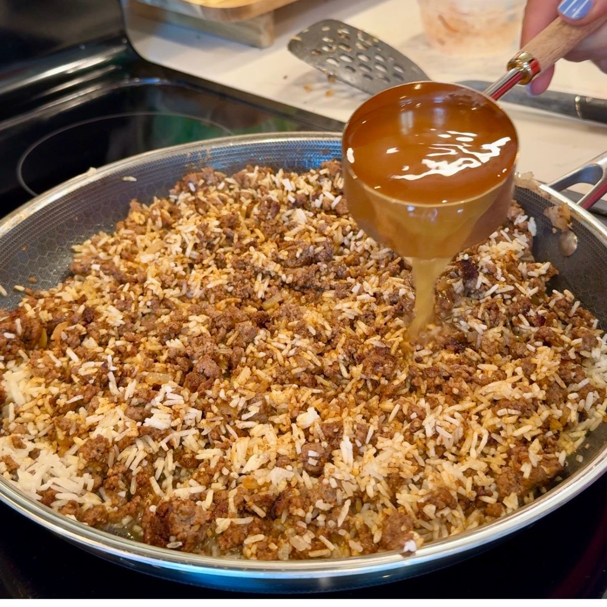 beef broth poured in measuring cup over beef and rice