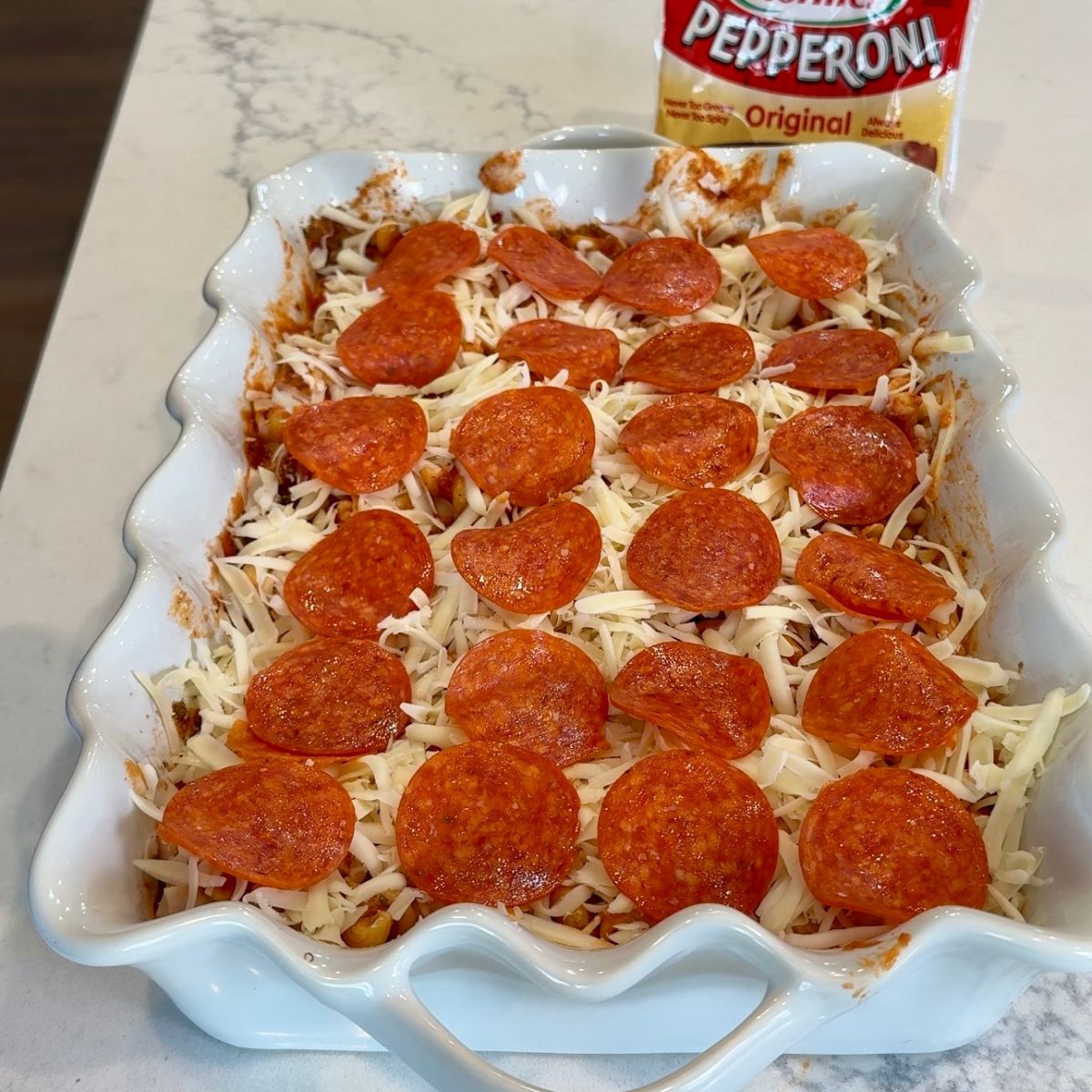 layer of pepperoni slices on top of pasta in white dish