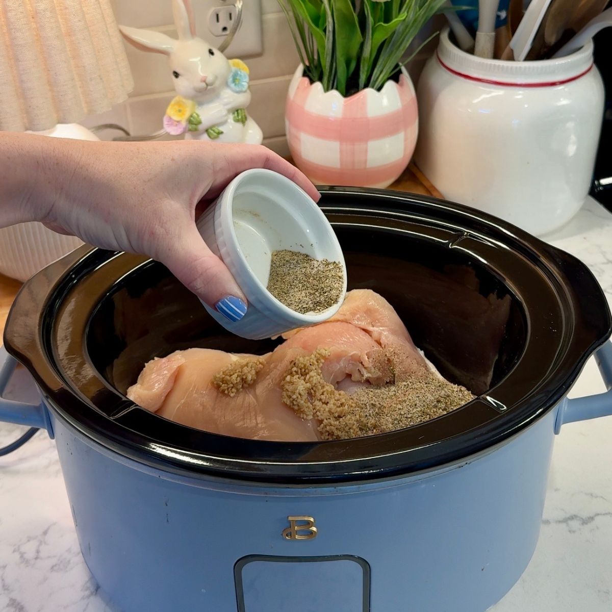 hand holding bowl of seasonings over chicken