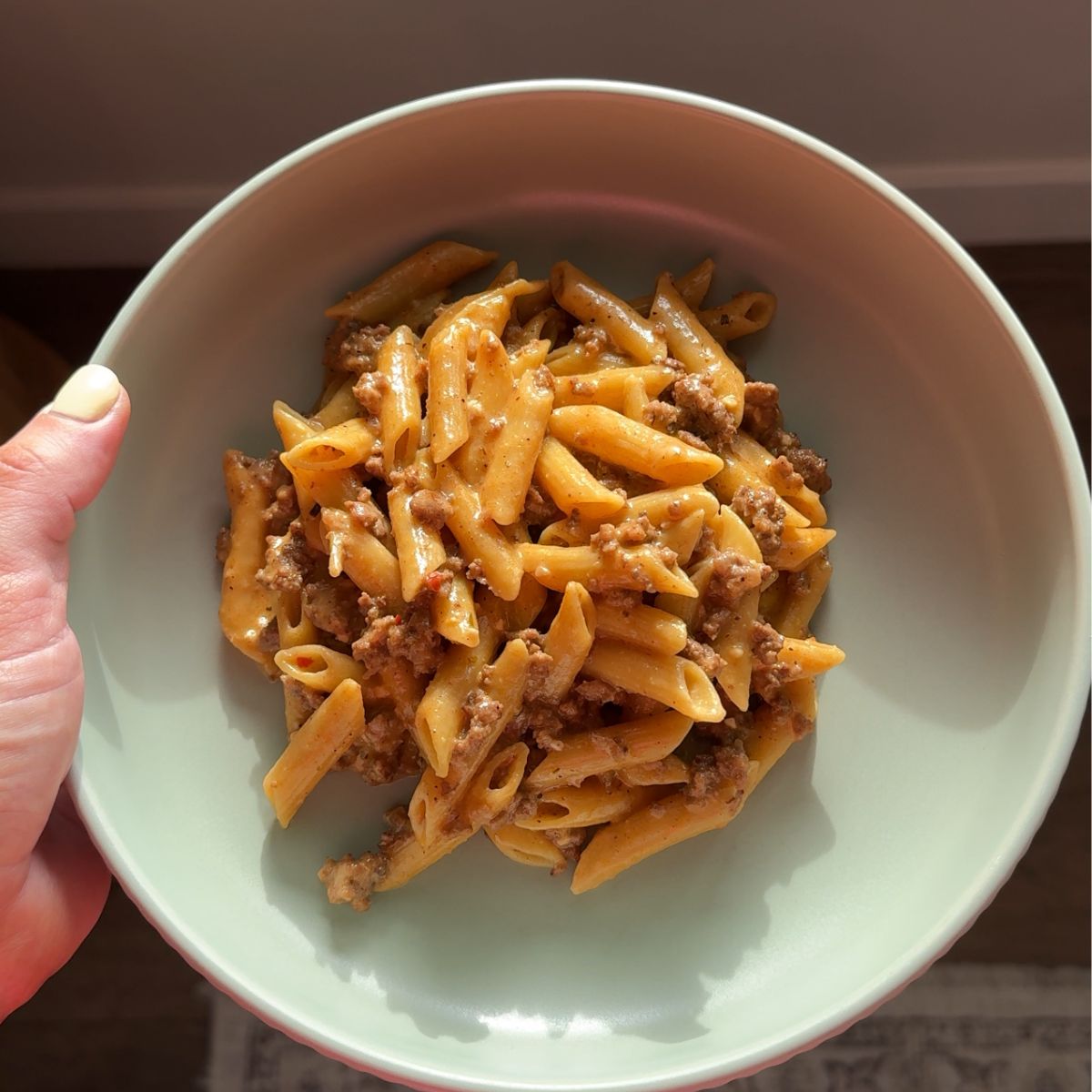 cowboy butter ground beef pasta on green plate with hand on left side