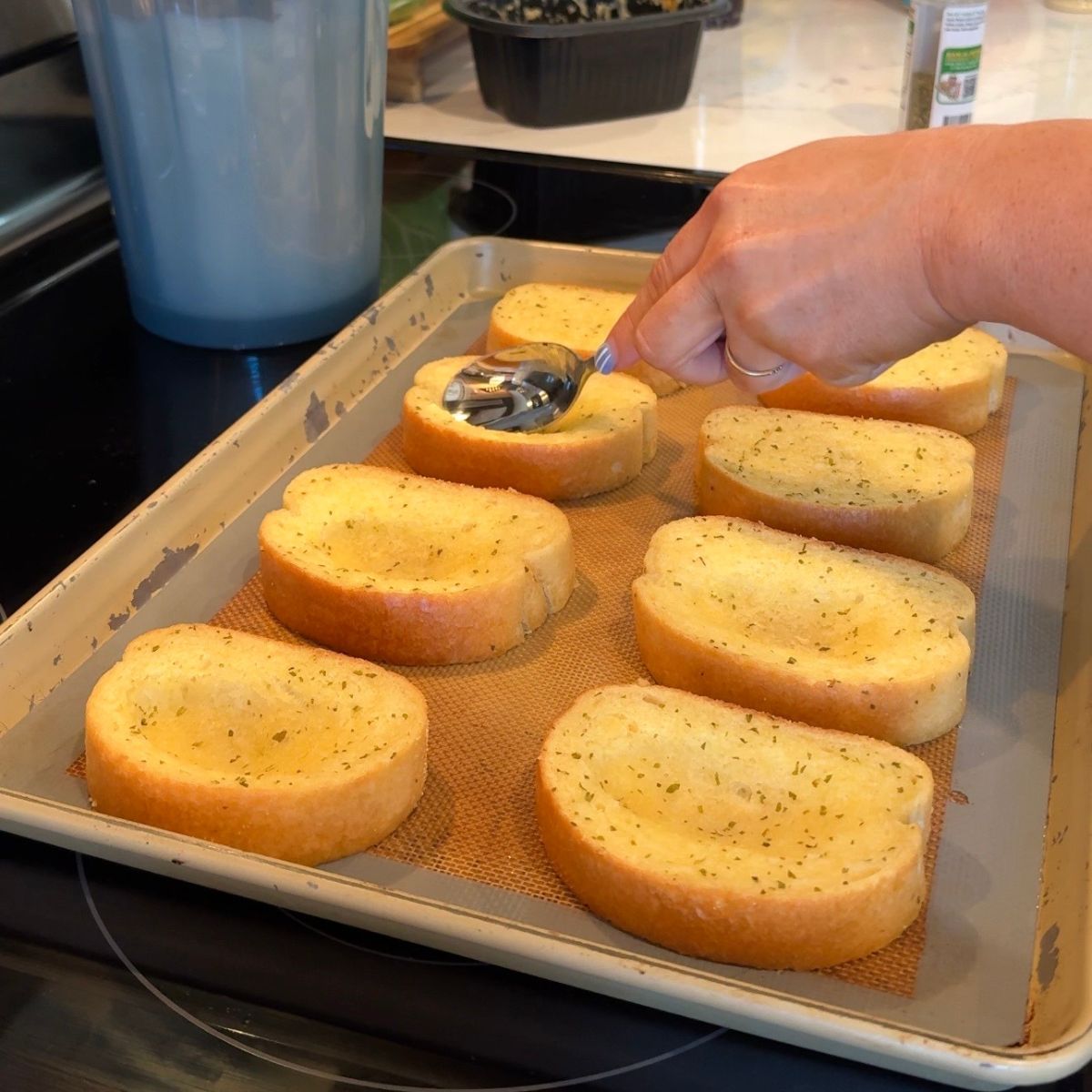 bread on pan with hand pressing spoon in middle of bread