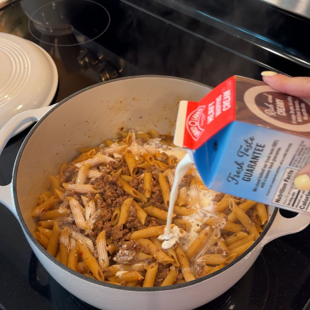 heavy cream carton pouring into pasta in dutch oven