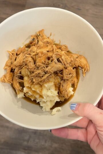 chicken over potatoes in bowl with hand