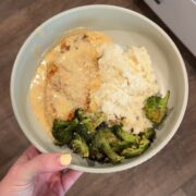 smothered cowboy butter chicken with broccoli, mashed potatoes on green plate with hand on left side