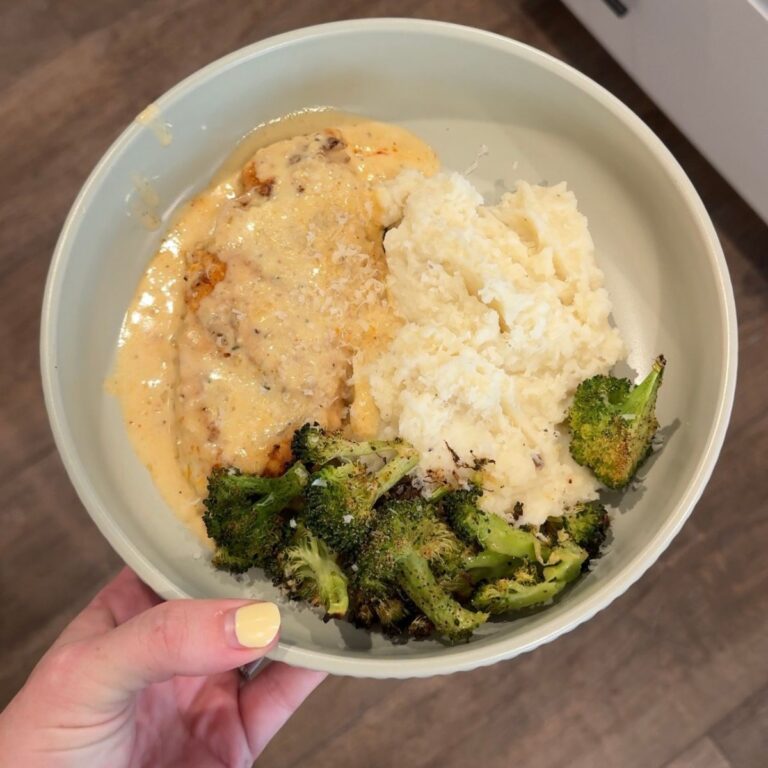 smothered cowboy butter chicken with broccoli, mashed potatoes on green plate with hand on left side