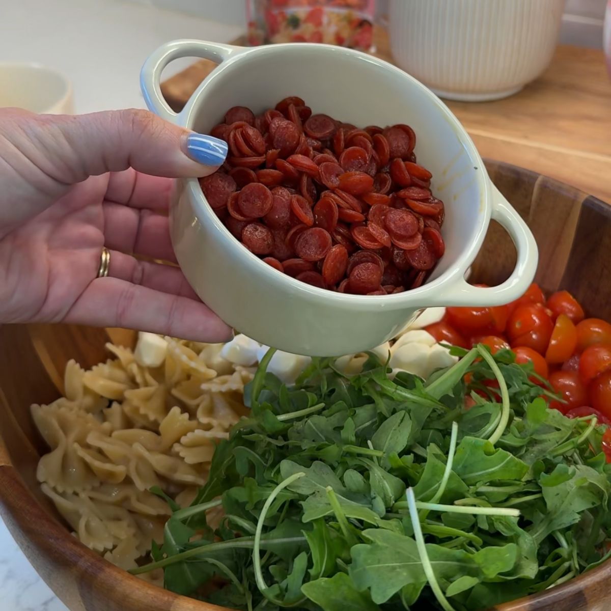hand holding mini pepperoni in bowl over pasta salad