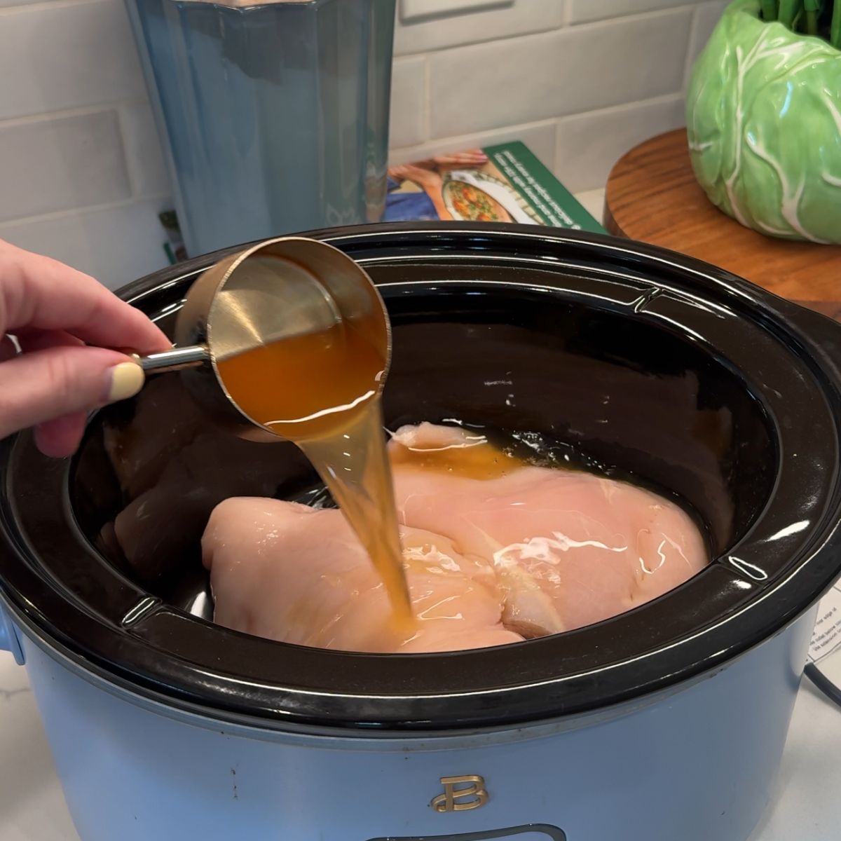 chicken in crockpot with hand holding cup with chicken broth