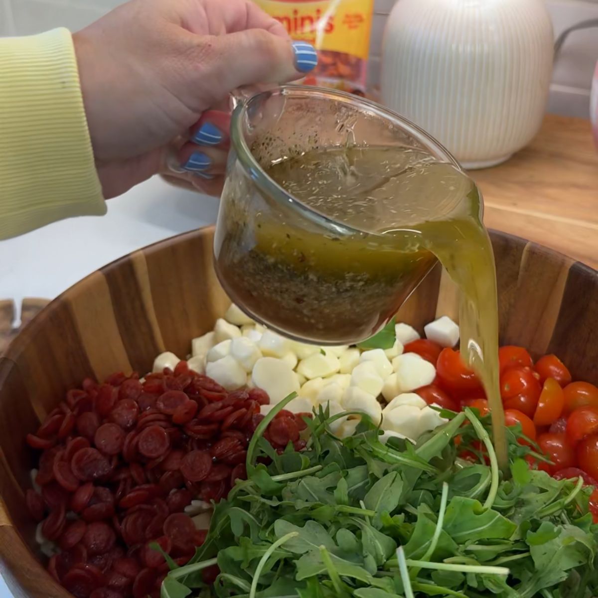 hand holding vinegarette dressing in cup pouring over pasta salad 