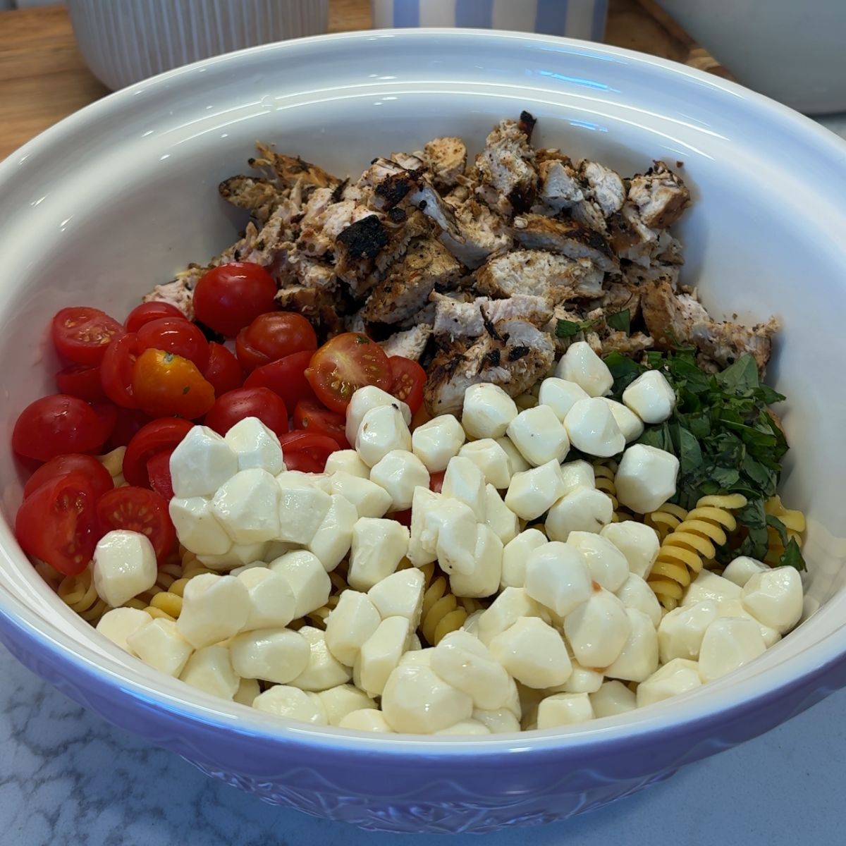 mozzarella, chicken, tomatoes, and basil on top of pasta in bowl