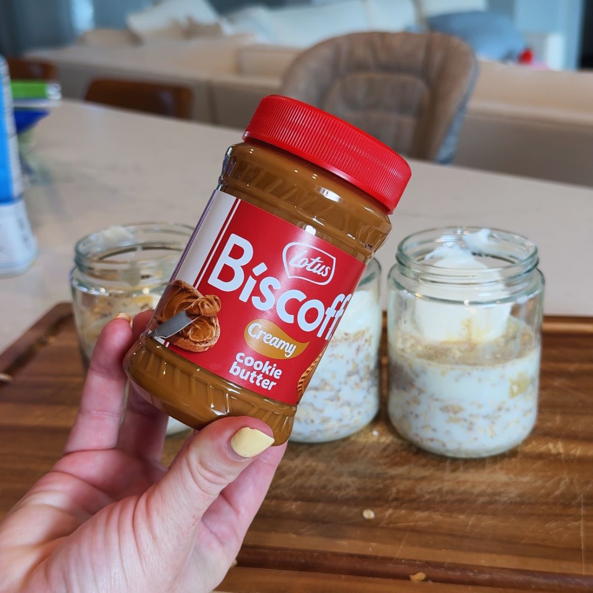 biscoff cookie butter jar in hand with 3 jars in background on wooden board