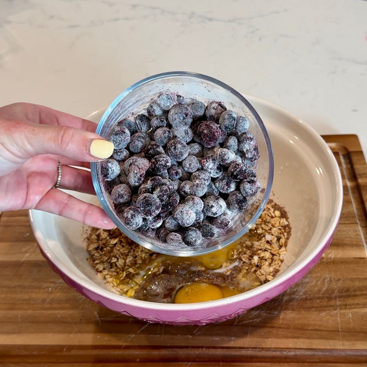 hand holding blueberries in container over mixing bowl