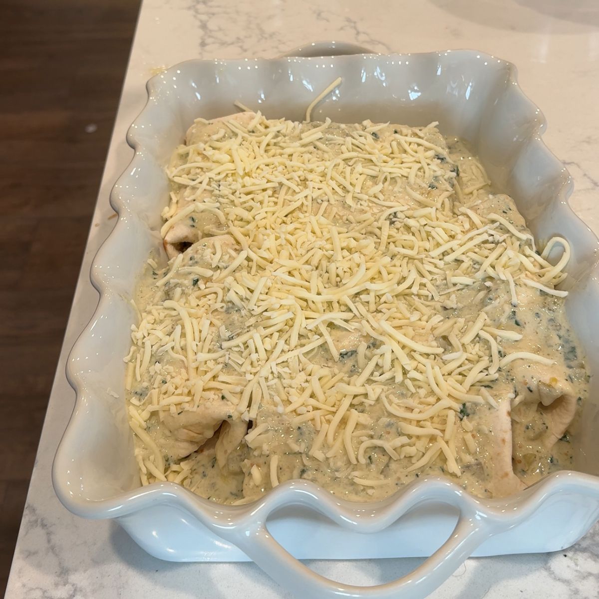 cheese on top of salsa verde mixture with tortillas in baking dish
