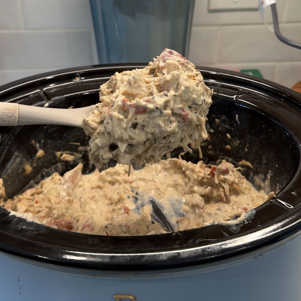 cooked chicken and cheese in crockpot, with spoon holding mixture over slow cooker