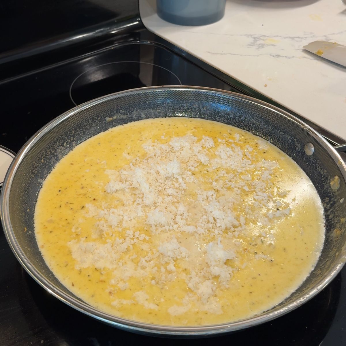 grated parmesan cheese on top of cream sauce in skillet 