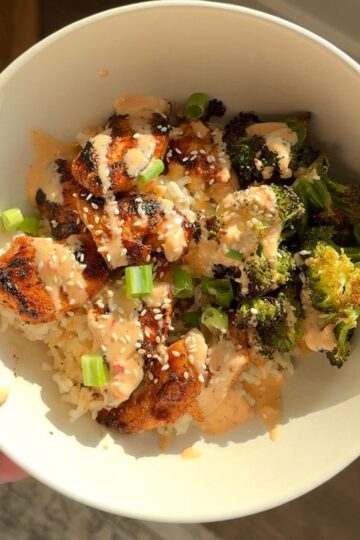 bang bang chicken with broccoli and rice in bowl and hand holding bowl