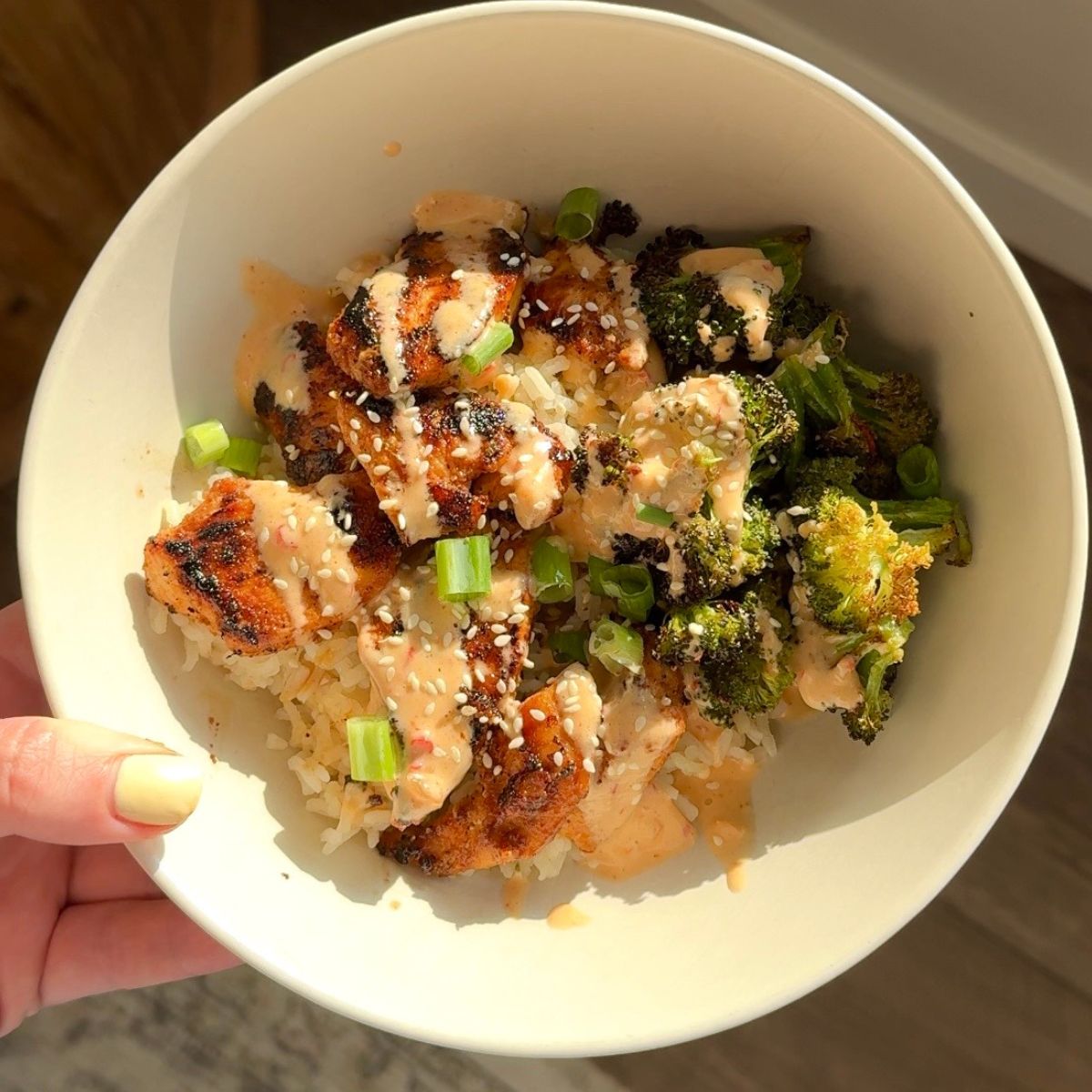bang bang chicken with broccoli and rice in bowl and hand holding bowl