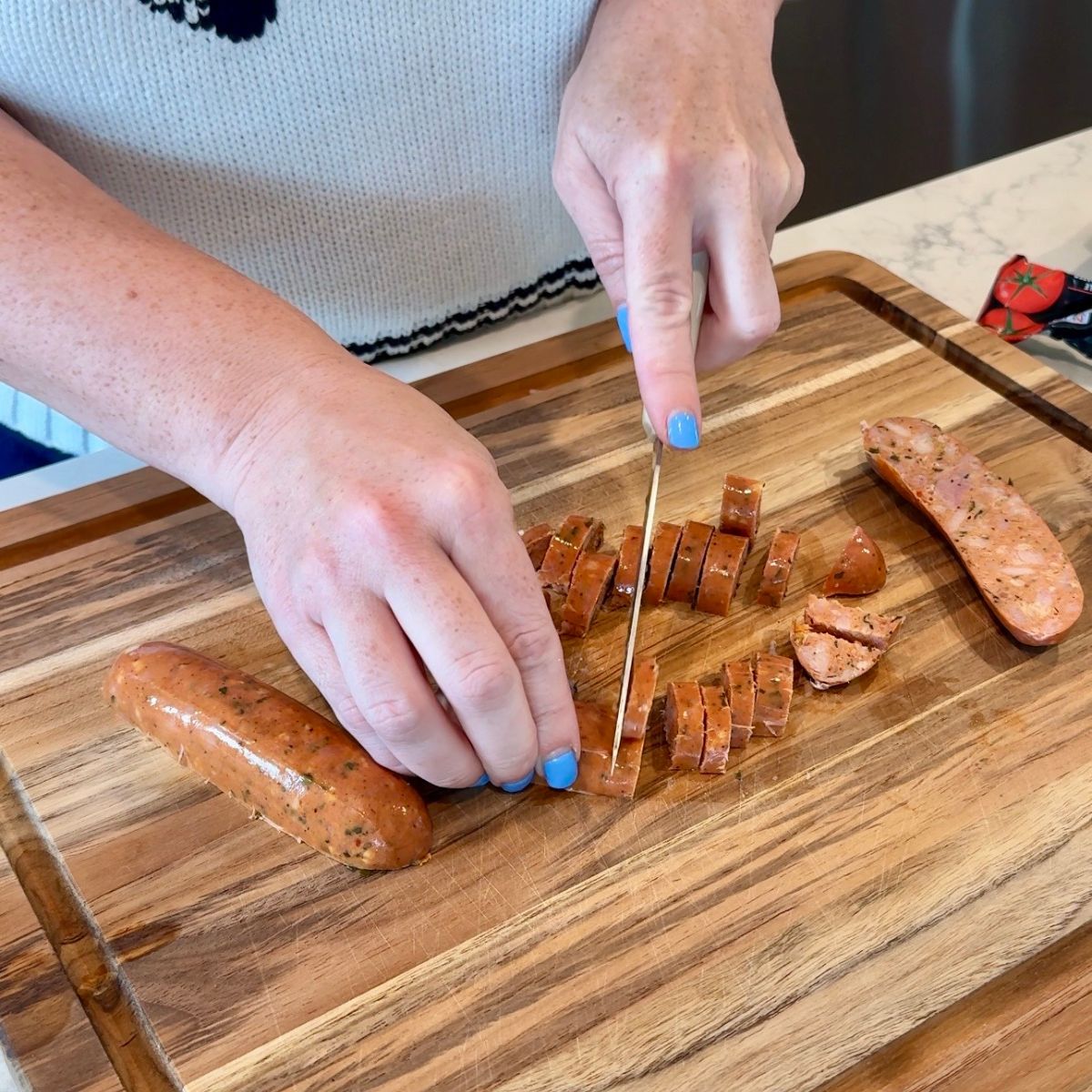 person cutting chicken sausage on wooden cutting board