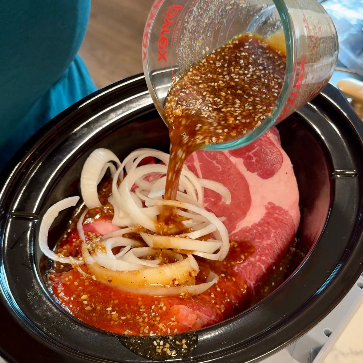 beef, onions in crockpot. sauce being poured on top