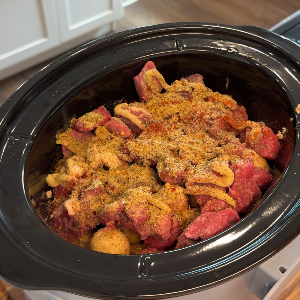 seasonings on meat and potatoes in black slow cooker