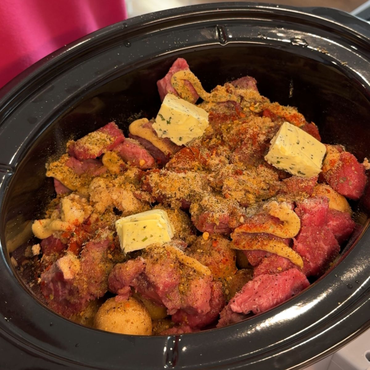 butter on seasonings and meat and potatoes in crockpot
