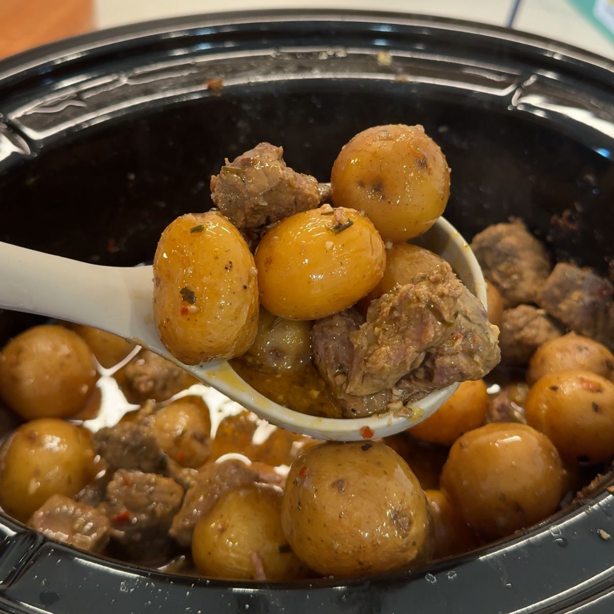 steak and potatoes in crockpot with spoon holding ingredients