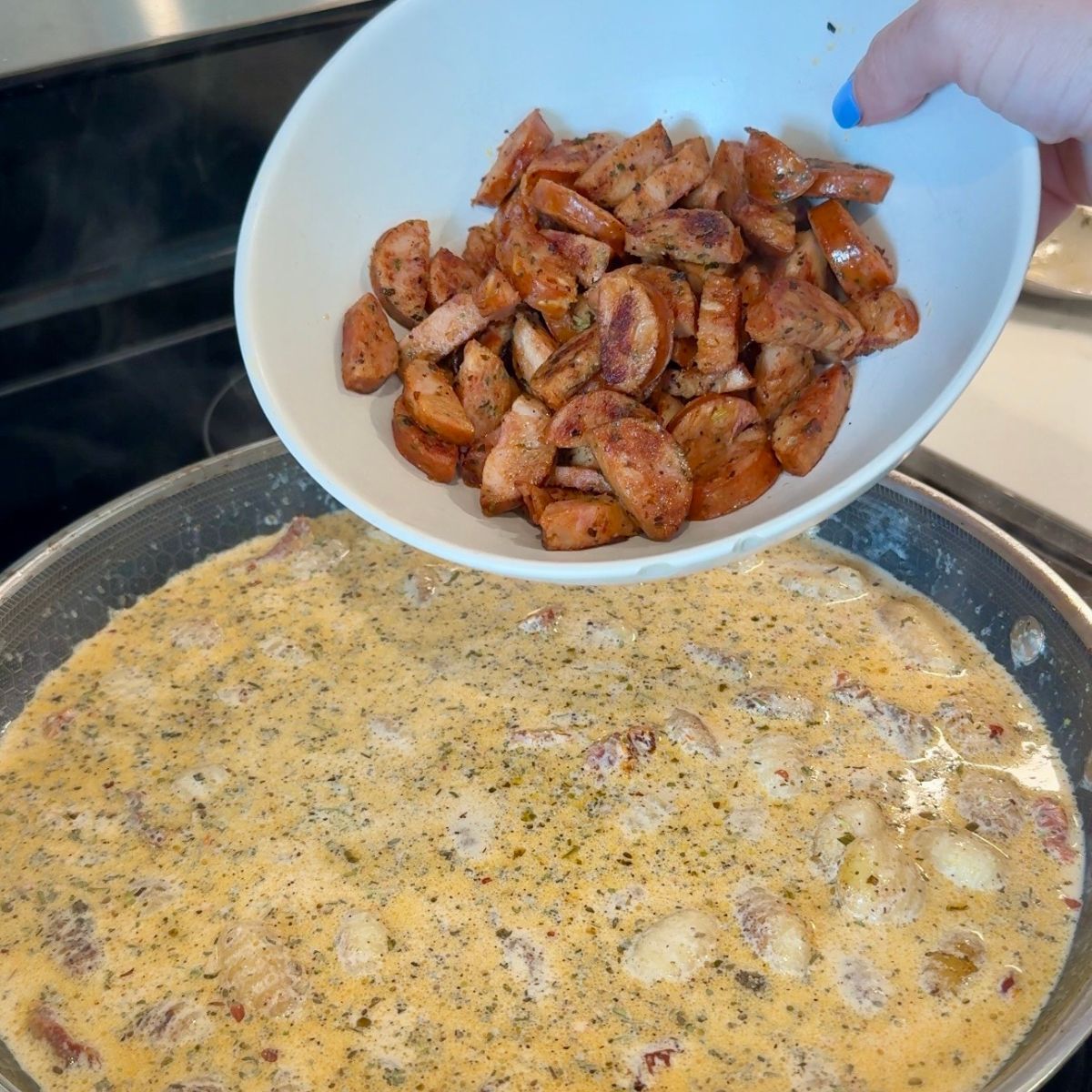 cooked chicken sausage in bowl over skillet with creamy sauce