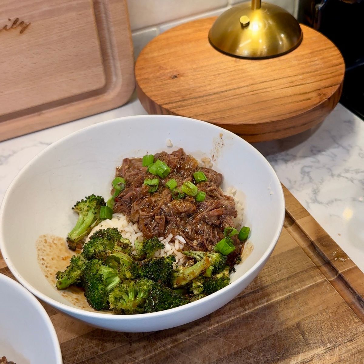 beef, broccoli, green onions and rice in cream bowl on wooden board with lamp in background
