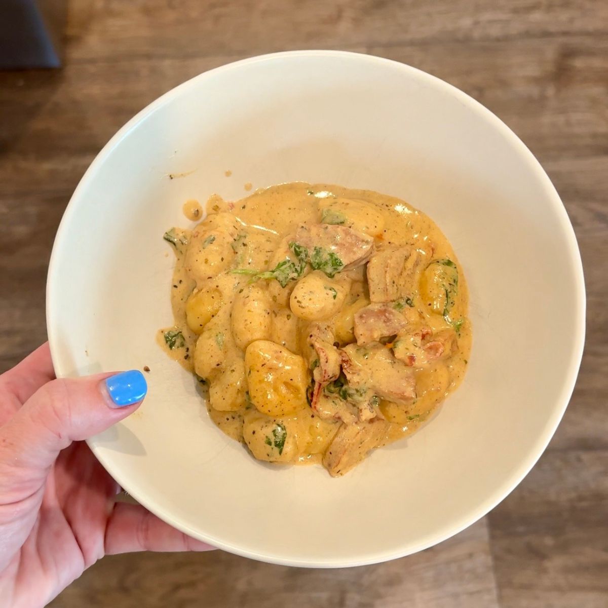creamy marry me sausage gnocchi in bowl with hand on left side holding bowl