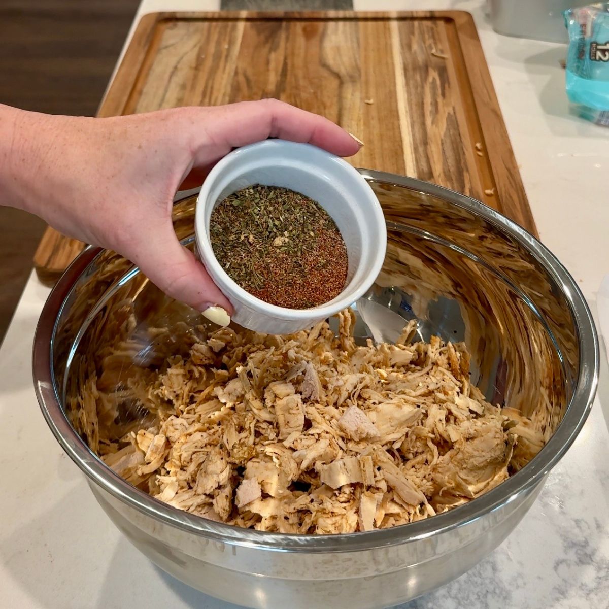 chicken in mixing bowl with hand holding seasonings