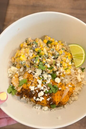 chicken street corn bowl in cream bowl with hand holding it