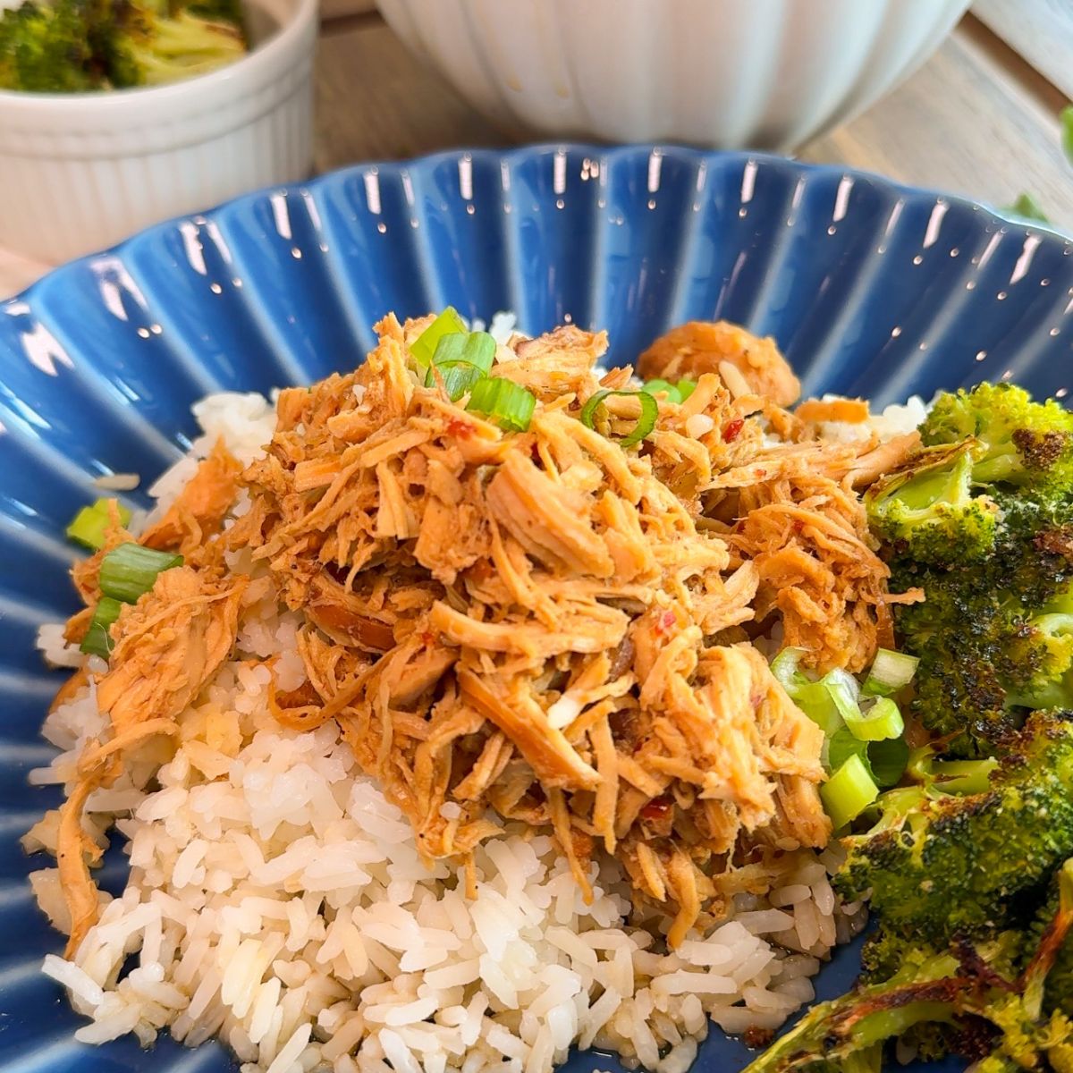 crockpot mongolian chicken on blue plate with rice, broccoli and green onions. white cup with broccoli in background